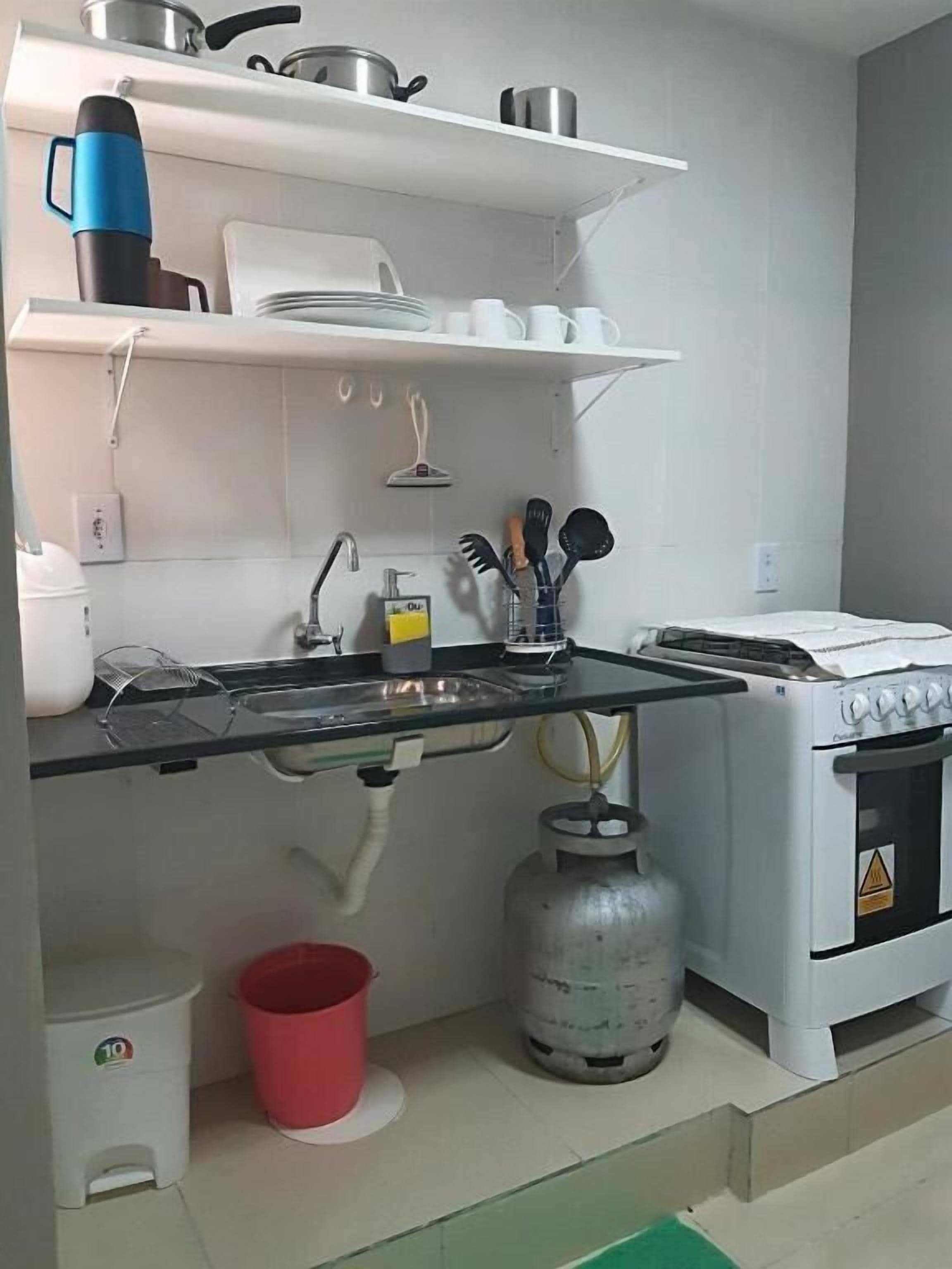 A kitchen with a gas stove, a gas cylinder, a sink, and various utensils.