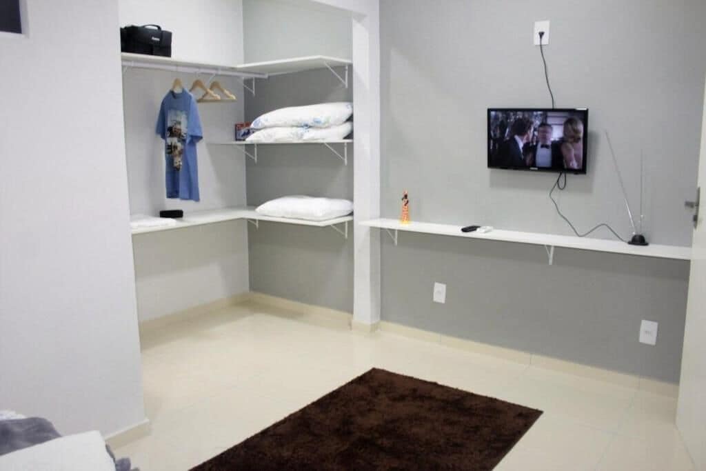 Una habitación con un armario blanco, un televisor montado y un tapete marrón.
