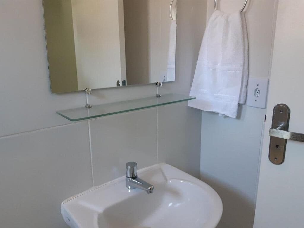 A bathroom with a white sink, a glass shelf above it, and a mirror.