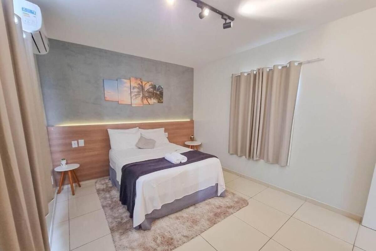 A modern hotel room with a large bed, a small side table, a wall-mounted air conditioning unit, and a curtain on the window.