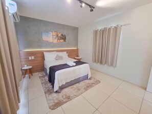 Una habitación de hotel moderna con una cama grande, una mesita auxiliar pequeña, un equipo de aire acondicionado instalado en la pared y una cortina en la ventana.