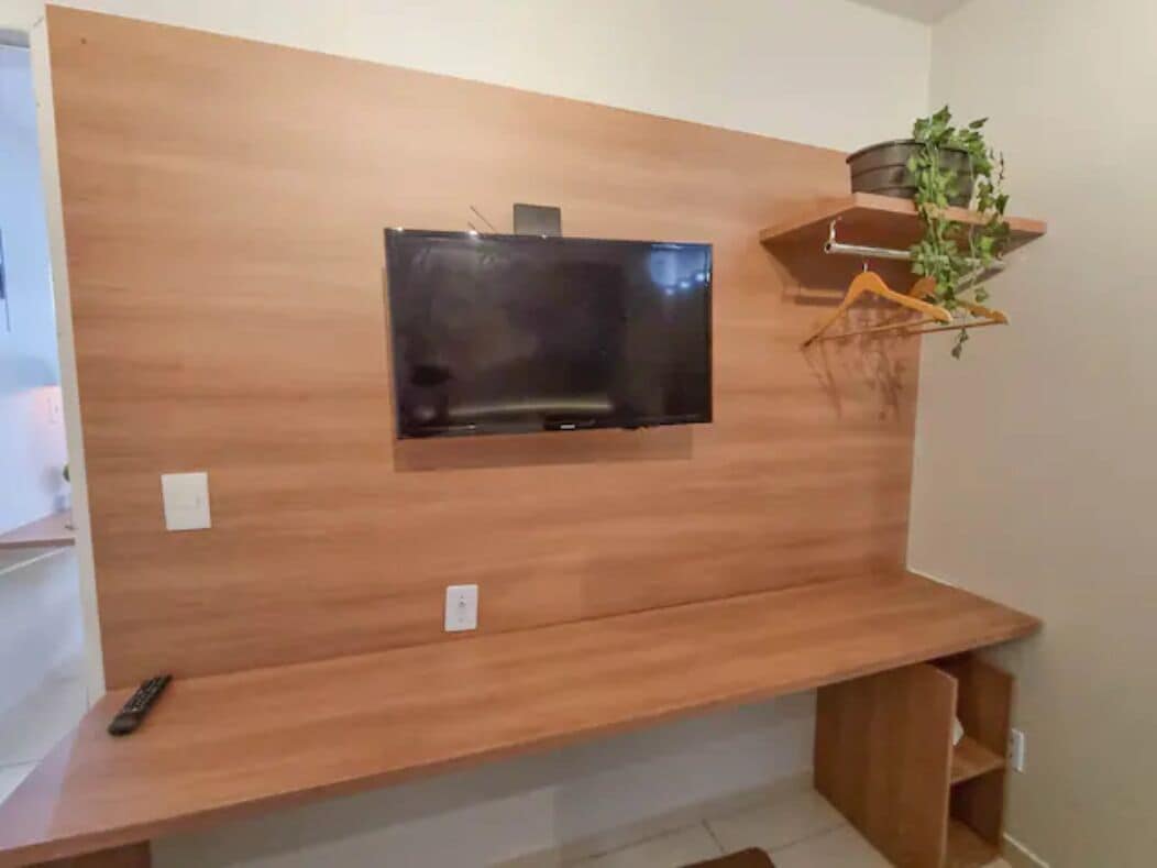 Una sala de estar moderna con un televisor de pantalla plana montado en una pared de madera, un estante pequeño con una planta y un control remoto en el suelo.