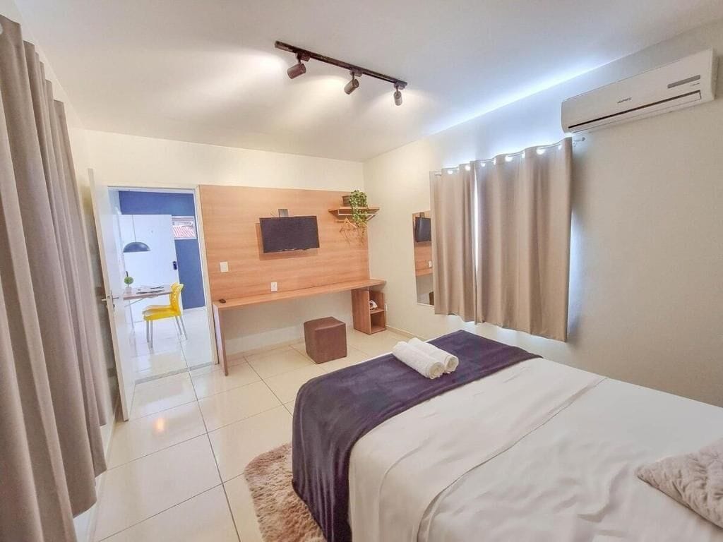 A modern hotel room with a bed, a desk, a chair, a TV, and an air conditioning unit.
