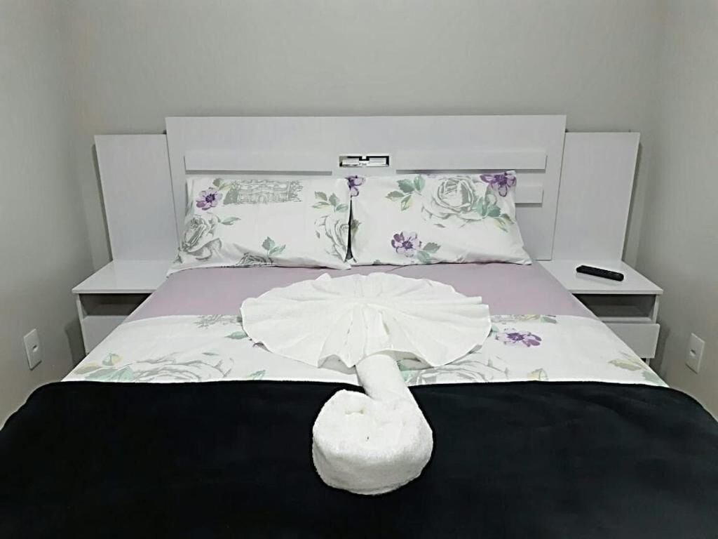 A neatly made bed with a white duvet, a black blanket, and a white decorative item resembling a fan.