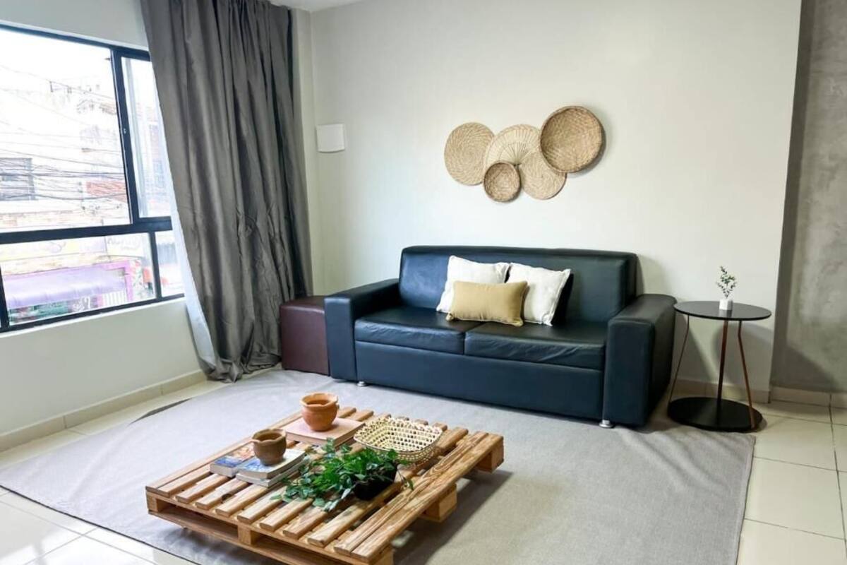 A modern living room with a dark blue sofa, a wooden coffee table with books and a plant, and a decorative wall piece.