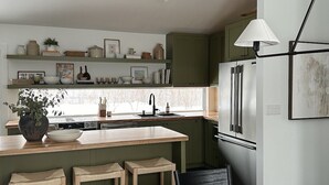 Een moderne keuken met een centraal eiland, groene kastjes en een roestvrijstalen koelkast.