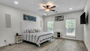 A bedroom with a bed, a ceiling fan, two windows, and artwork on the walls. - Waterfront house on Sam Rayburn (Brookeland)