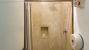 A bathroom with a shower, a toilet, a towel dispenser, and a small shelf with a box. - Sac Ek Hotel (Valladolid)