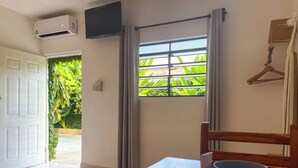 A room with a wooden table, a remote control, a white mug, a TV mounted on the wall, and a window with curtains. - Sac Ek Hotel (Valladolid)