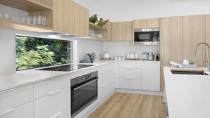 Une cuisine moderne avec des meubles blancs, un four encastré, un four à micro-ondes et une grande fenêtre donnant sur un paysage verdoyant.
