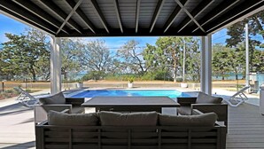 Un espace piscine extérieur doté d’une terrasse en bois, de chaises longues et d’un coin salon couvert avec des coussins.