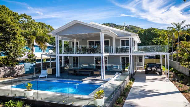 Une maison à deux étages dotée d’une piscine, d’un patio couvert et offrant une vue sur la verdure environnante.
