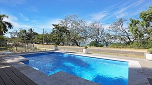 Une piscine rectangulaire à l’eau d’un bleu limpide, entourée d’une terrasse en bois et d’un chemin pavé.