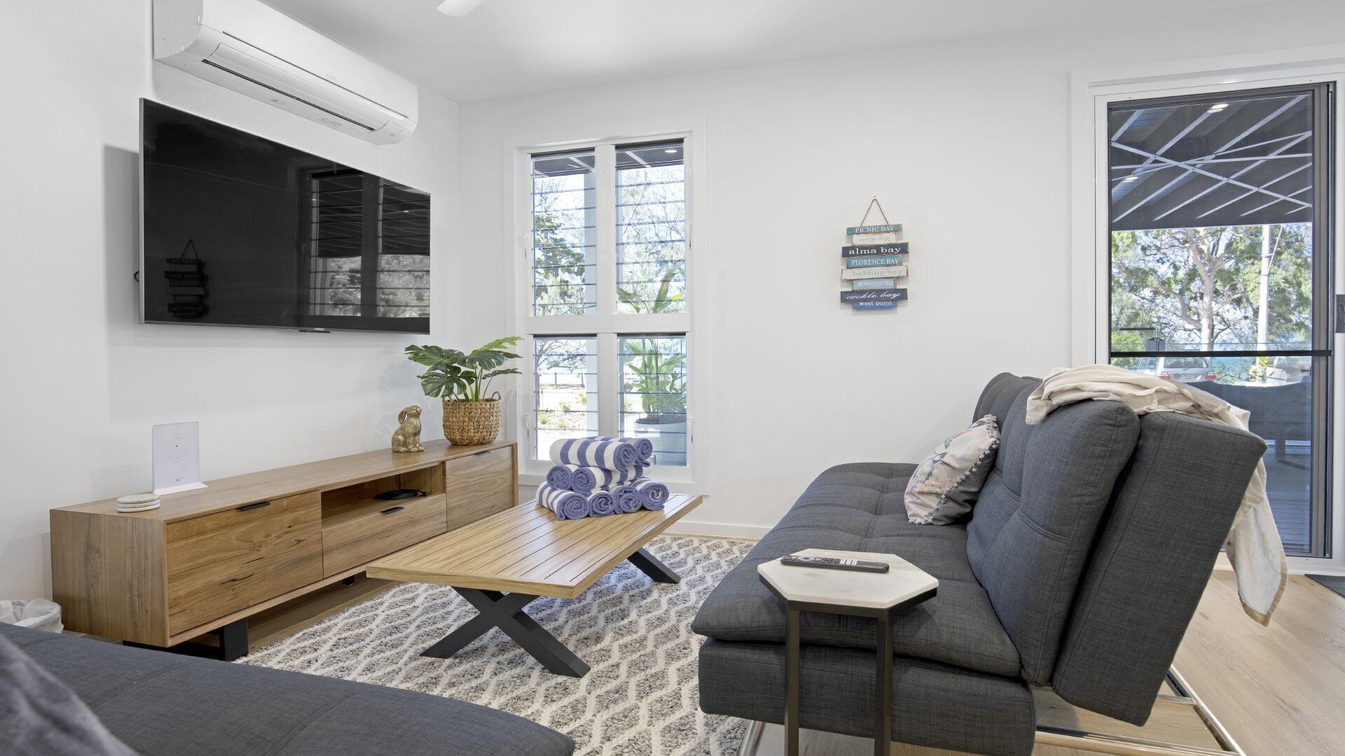 Una sala de estar moderna con un sofá gris, una mesa de centro de madera y un televisor montado en la pared.