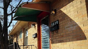 A brick building with a green awning, a red door, and a black mailbox with the number 1619. - The Big Apple City View with Balcony (Dayton)