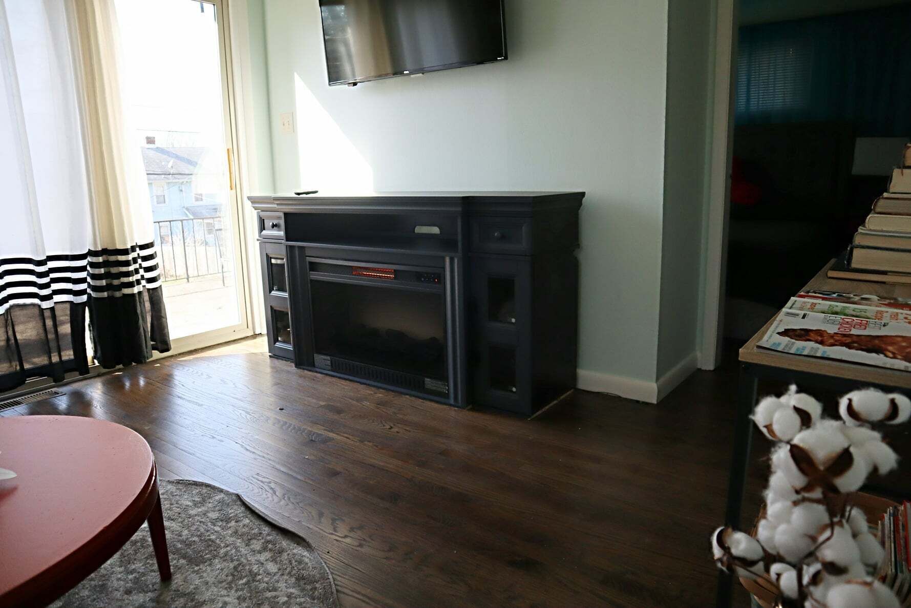 Una sala de estar con chimenea, un televisor montado encima, una mesa de comedor con sillas y una ventana con cortinas.