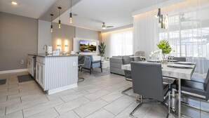 A modern kitchen with a central island, a dining area with a table and chairs, and a living room with a sofa and a TV.