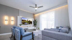 A modern living room with a flat-screen TV, grey sofas, and a ceiling fan.