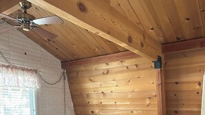 Un dormitorio con techo de madera, una cama con ropa de cama blanca, una mesita de noche con lámpara y un pequeño banco de madera.