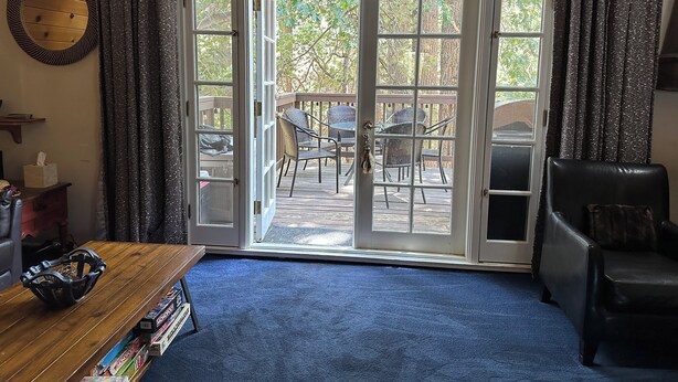 Una habitación con una mesita de centro de madera, una butaca de cuero negro y vistas a una terraza exterior con sillas y una mesa.