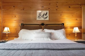 A wooden-paneled room with a bed, two bedside lamps, and a framed leaf artwork on the wall. - Fern Cabin - Hot Tub & Mountain Views - Dog Friendly! (Blue Ridge)