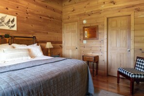 A wooden room with a bed, a chair, a nightstand, and a door. - Fern Cabin - Hot Tub & Mountain Views - Dog Friendly! (Blue Ridge)