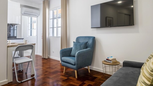 Un salon moderne avec un canapé gris, un fauteuil bleu et une petite table ronde sur laquelle sont posés des livres.