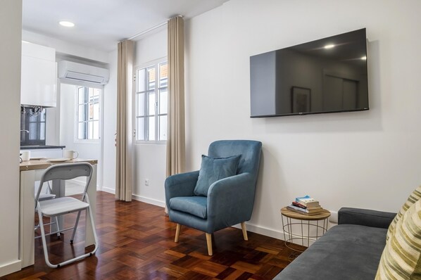 A modern living room with a grey sofa, a blue armchair, and a small round table with books. - Ribeira do Esmeraldo 3B by Homie (Funchal)