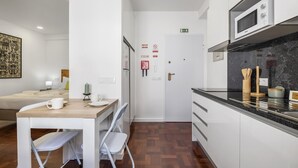 Une chambre d’hôtel compacte comprenant un coin cuisine, un espace repas avec une table et des chaises, un lit et une grande œuvre d’art accrochée au mur.