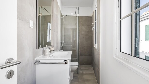 Et moderne badeværelse med en glasvæg omkring brusenichen, en hvid vask og et toilet.