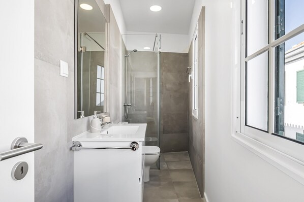 Een moderne badkamer met een douchecabine van glas, een witte wastafel en een toilet.