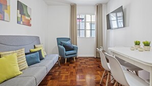 Ein modernes Wohnzimmer mit grauem Sofa, blauem Sessel und weißem Esstisch.
