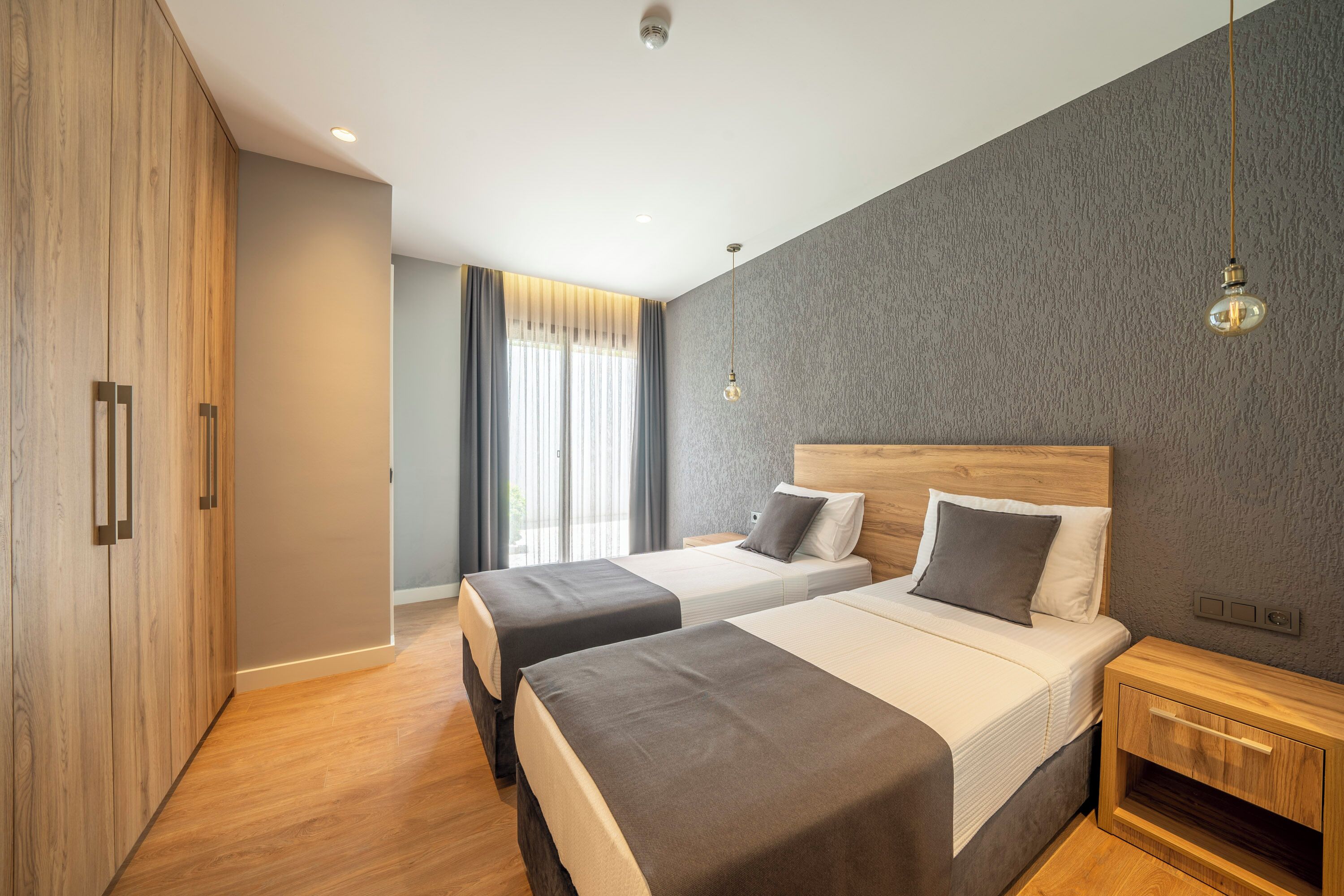 Een moderne hotelkamer met twee bedden, een houten garderobe en een groot raam met gordijnen.