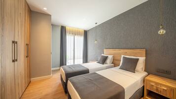 Een moderne hotelkamer met twee bedden, een houten garderobe en een groot raam met gordijnen.