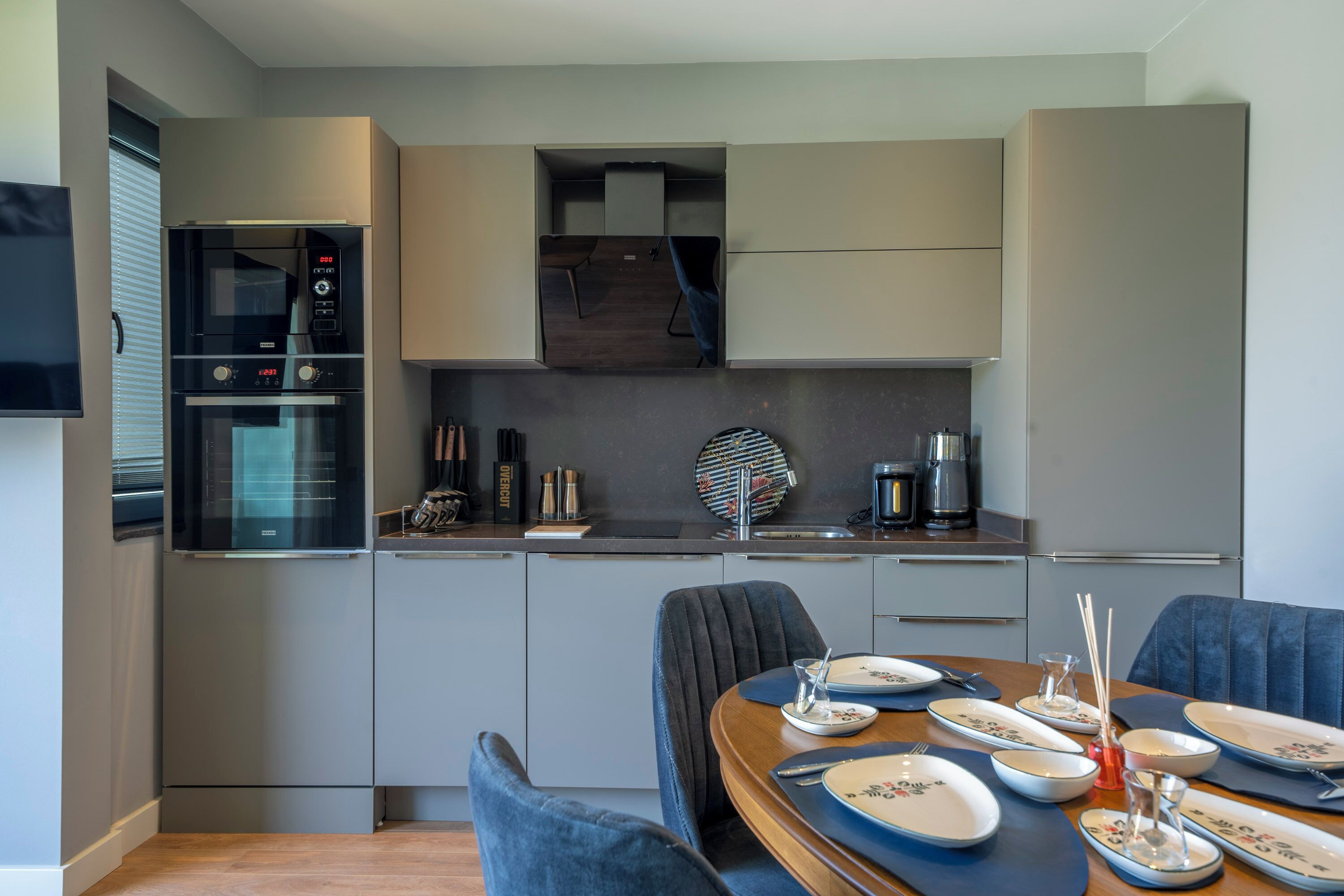 A modern kitchen with built-in appliances, a dining area with blue chairs, and a coffee machine.