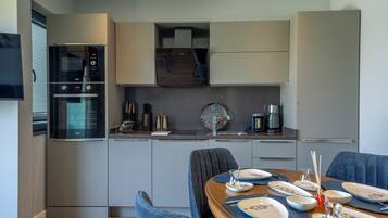 A modern kitchen with built-in appliances, a dining area with blue chairs, and a coffee machine.