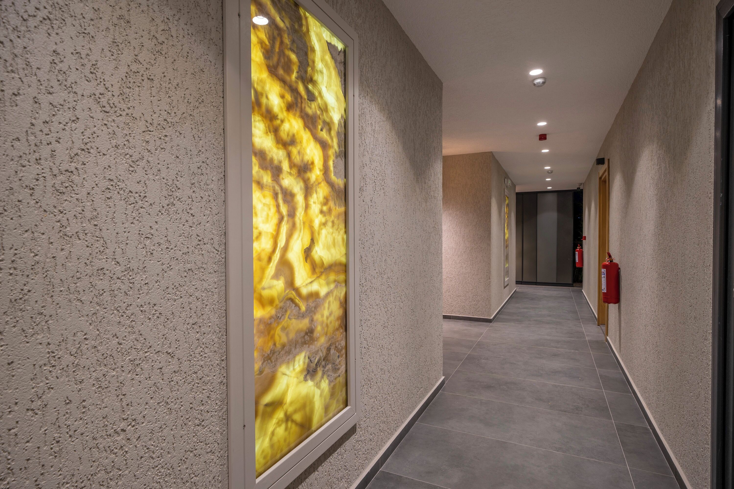 A hallway with textured walls, a large abstract artwork, and a fire extinguisher mounted on the wall.