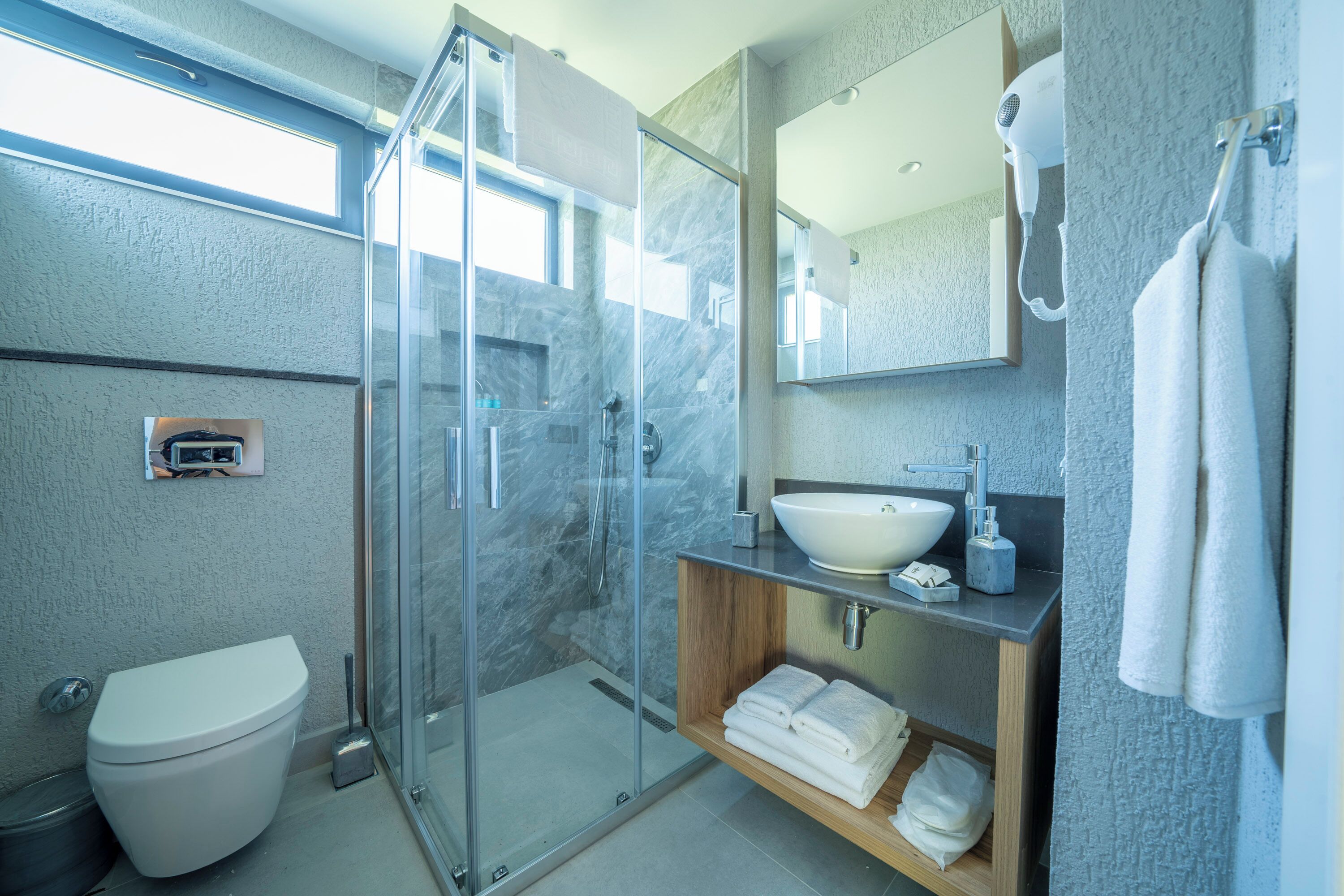 Een moderne badkamer met een glazen douchecabine, een wit toilet, een wastafel met een marmeren blad en een handdoekhouder.
