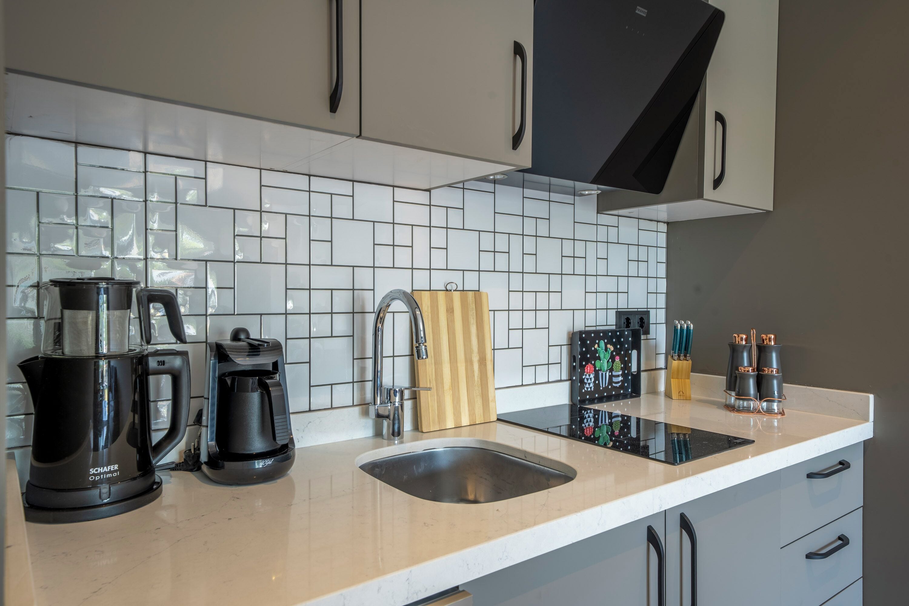 A modern kitchen with white tiled backsplash, stainless steel appliances, and a black coffee maker.