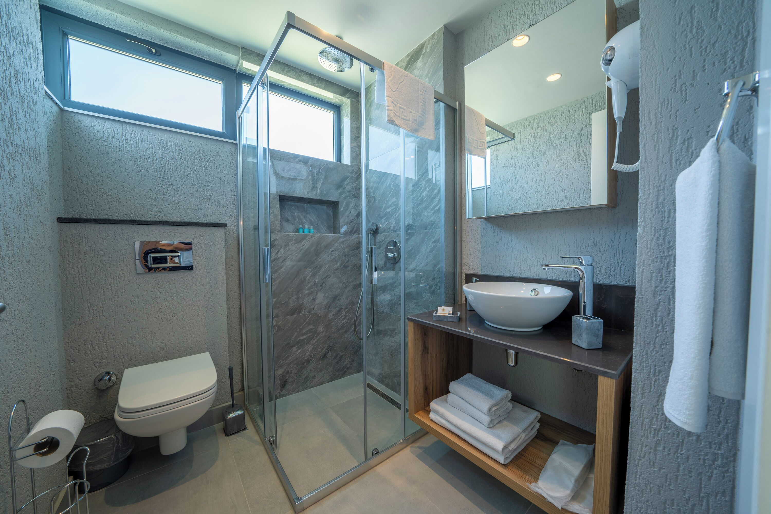 A modern bathroom with a glass-enclosed shower, a toilet, a sink, and a mirror.