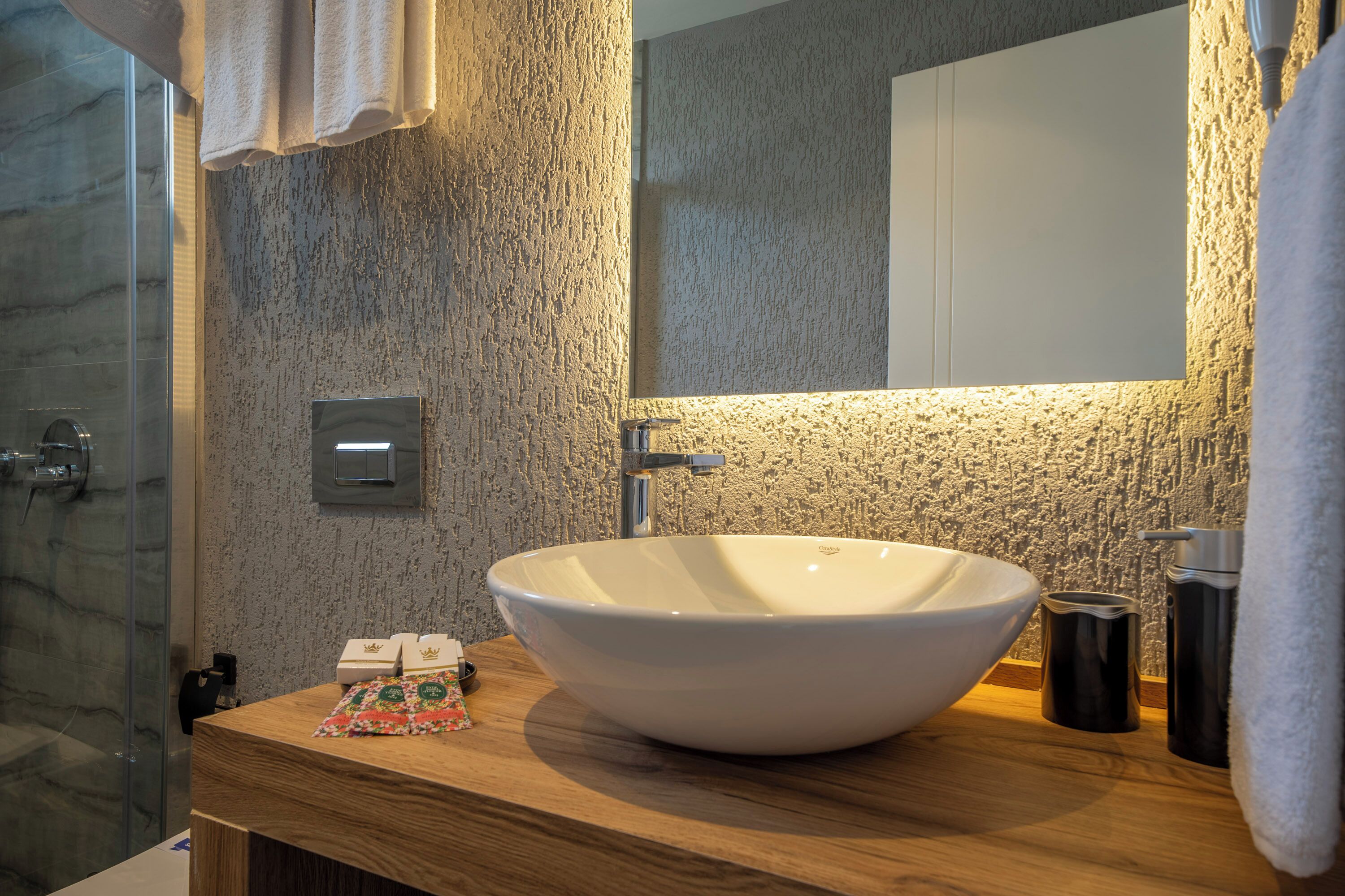 Un baño moderno con un lavabo blanco de diseño, encimera de madera y pared de piedra texturizada.