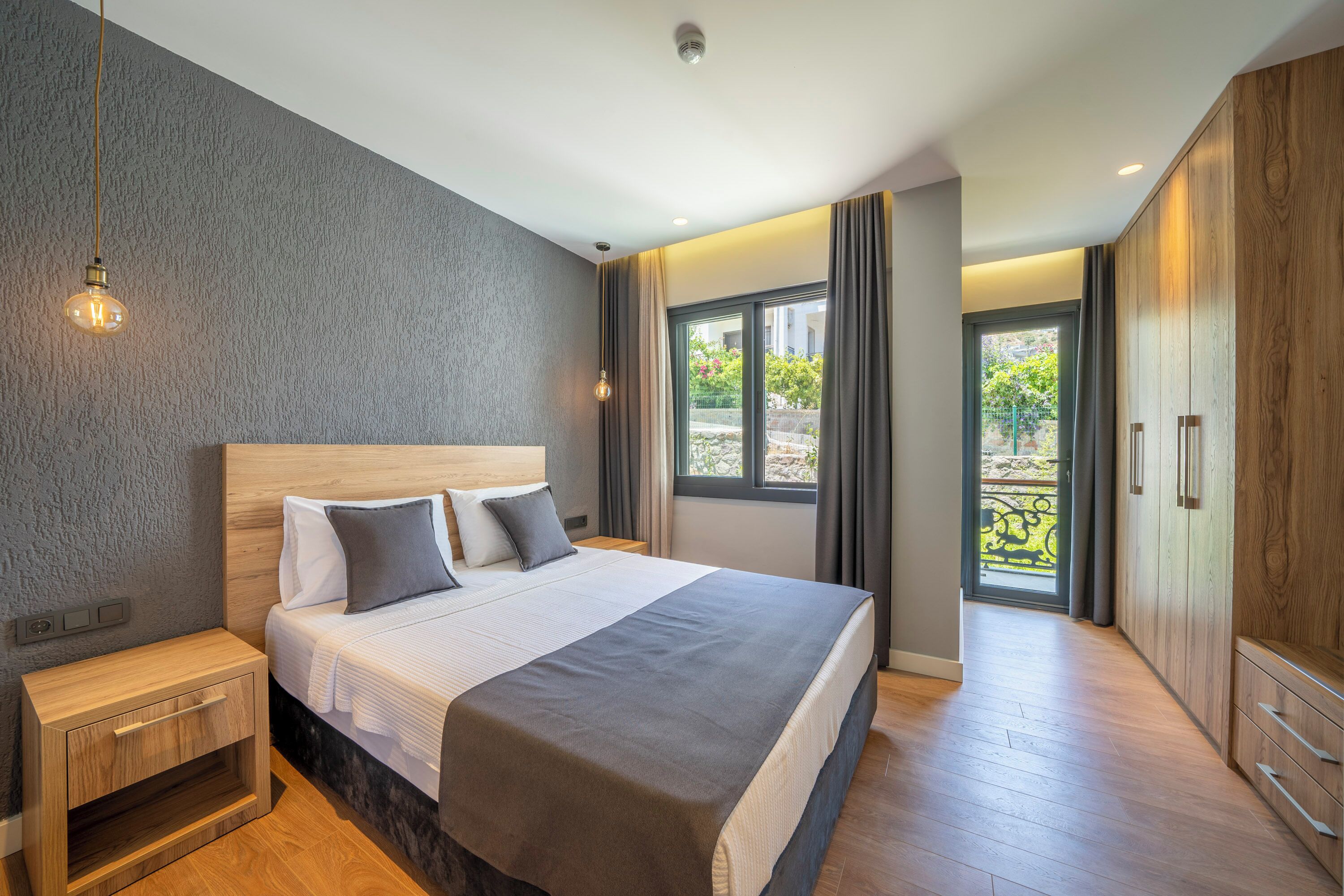 A modern bedroom with a large bed, wooden nightstands, and a wardrobe.