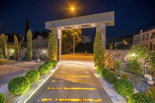 A well-lit entrance with a stone archway, a paved pathway, and neatly trimmed hedges.