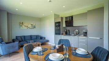 A modern living room with a sofa, a dining table set for four, and a kitchen area with appliances.