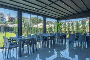 Un amplio comedor al aire libre con muebles modernos y ventanas grandes que ofrecen vistas del paisaje circundante.