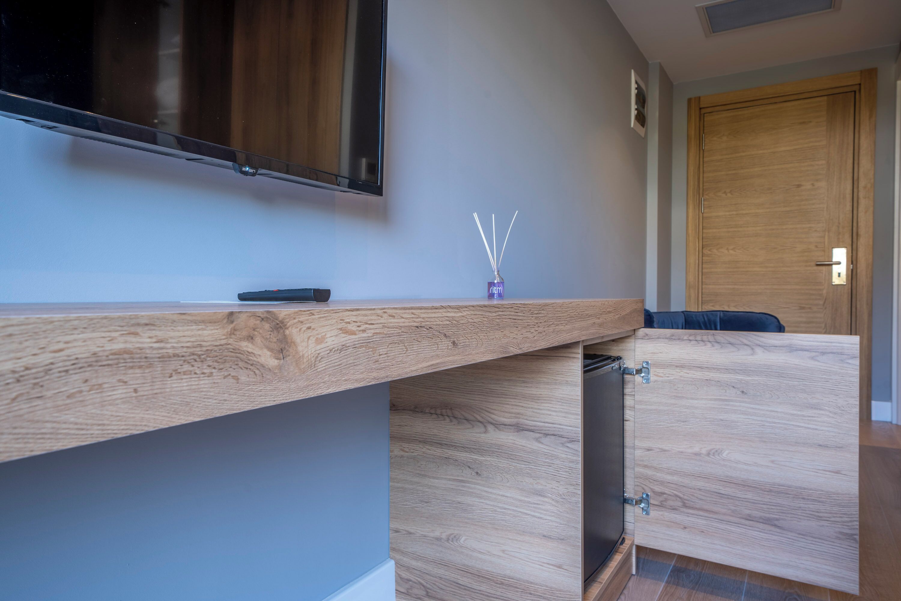 Una habitación moderna con un escritorio de madera, un televisor de pantalla plana montado en la pared y una puerta de madera.