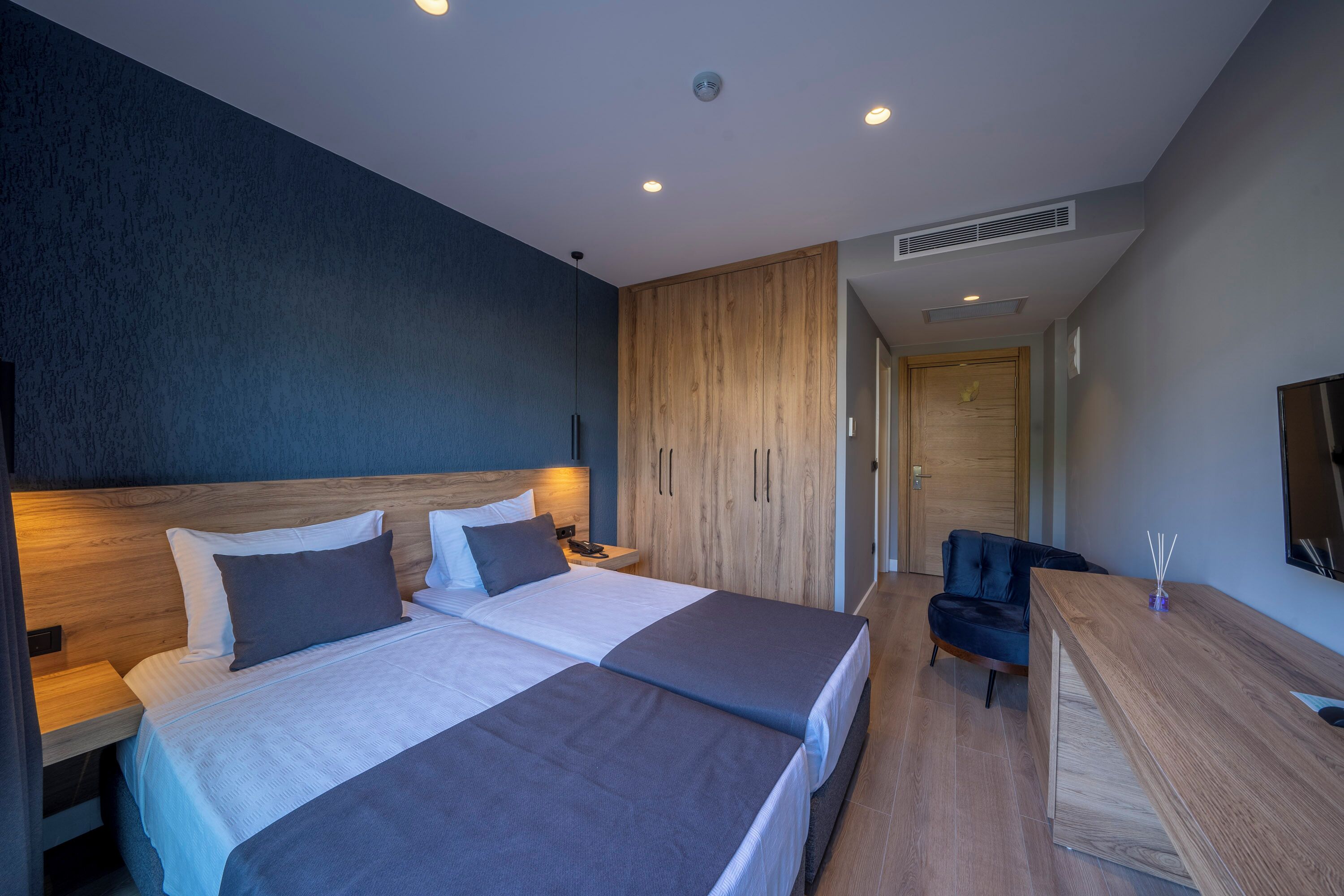 A modern hotel room with two beds, a desk, and a TV.