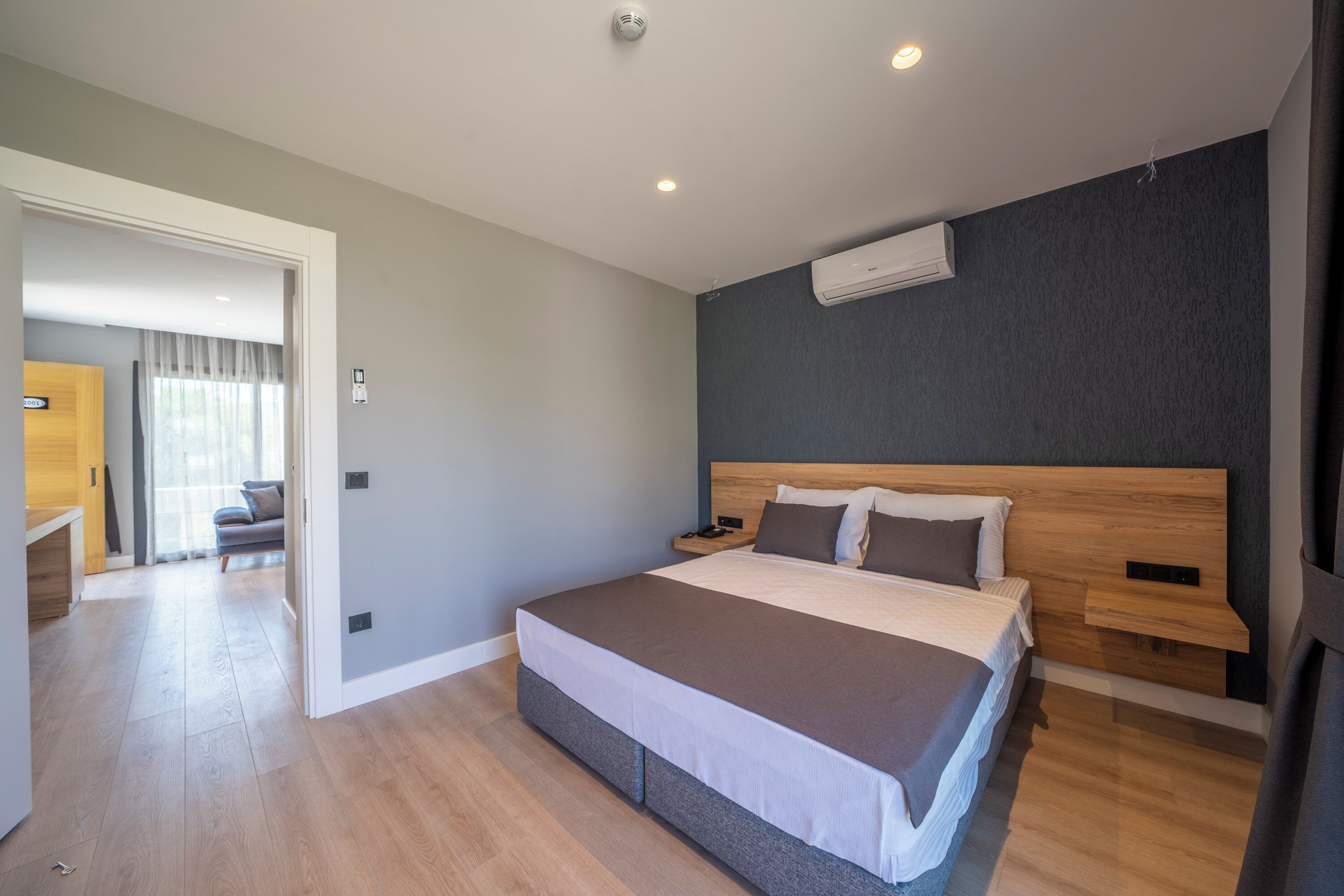 Een moderne hotelkamer met een groot bed, een houten hoofdbord, nachtkastjes en een airconditioning op de muur.
