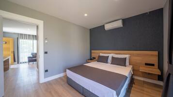 Een moderne hotelkamer met een groot bed, een houten hoofdbord, nachtkastjes en een airconditioning op de muur.