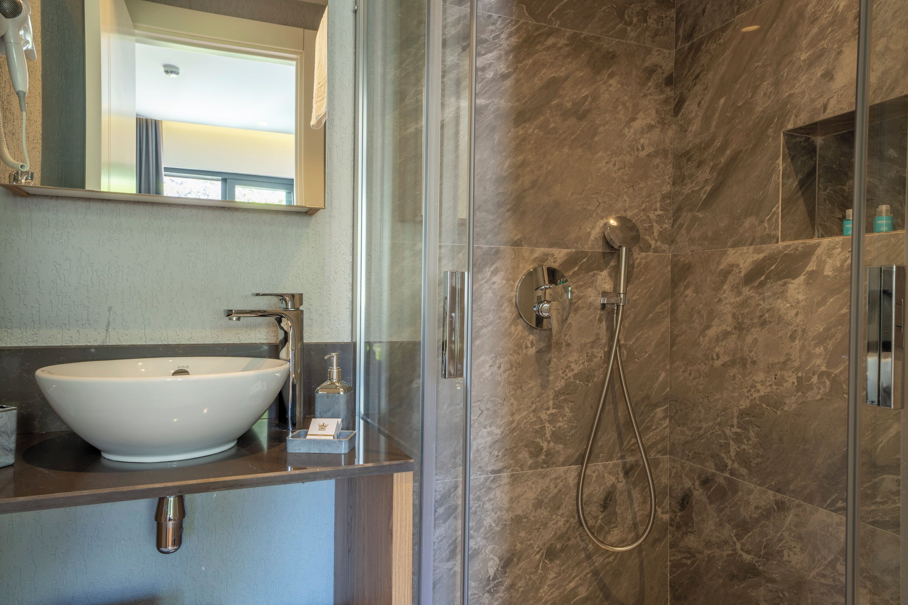 Une salle de bain moderne avec un grand lavabo blanc, une douche à parois de verre et un mur recouvert de carreaux de marbre.
